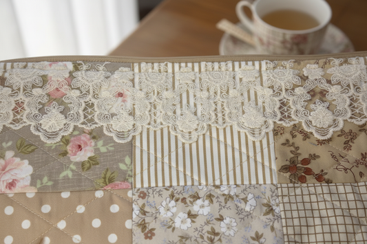 Close-up of handmade quilted patchwork fabric featuring vintage florals, lace trim, stripes, and polka dots in neutral tones
