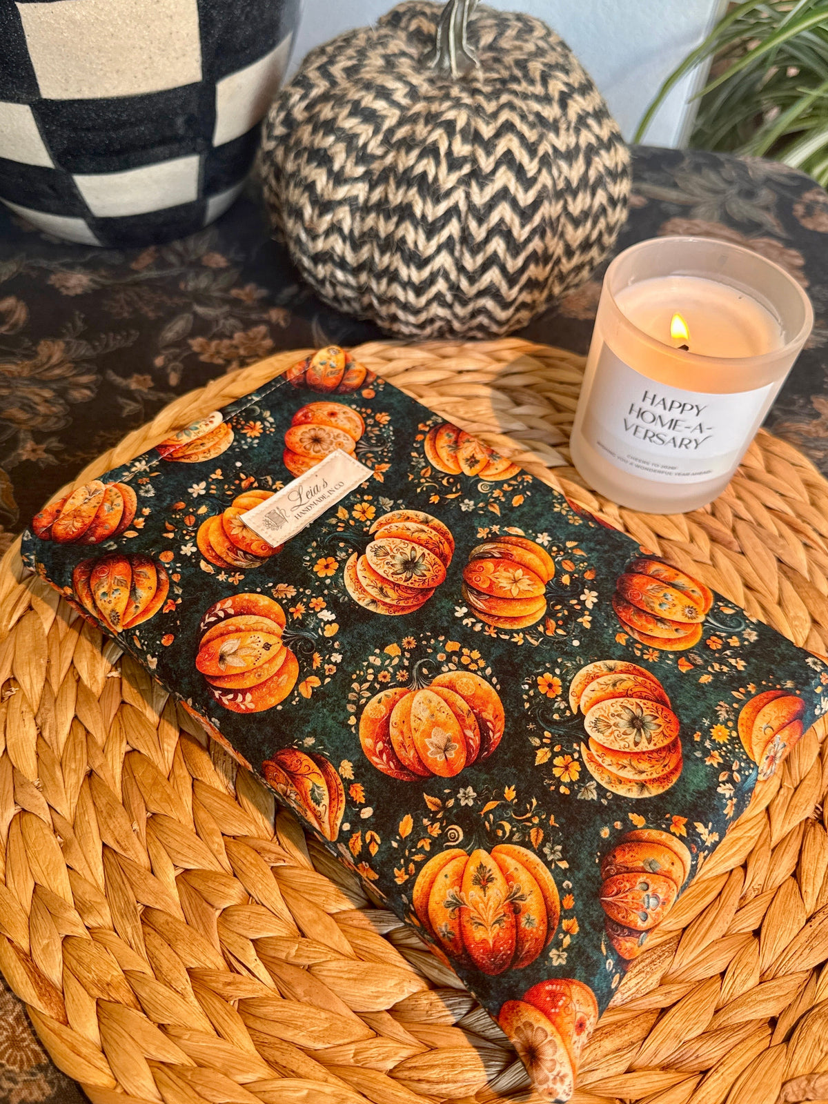 (flat lay, closed sleeve on wicker charger, overhead angle)
Handmade quilted book sleeve in Gilded Gourd pumpkin print, laying flat on a wicker charger with autumn décor