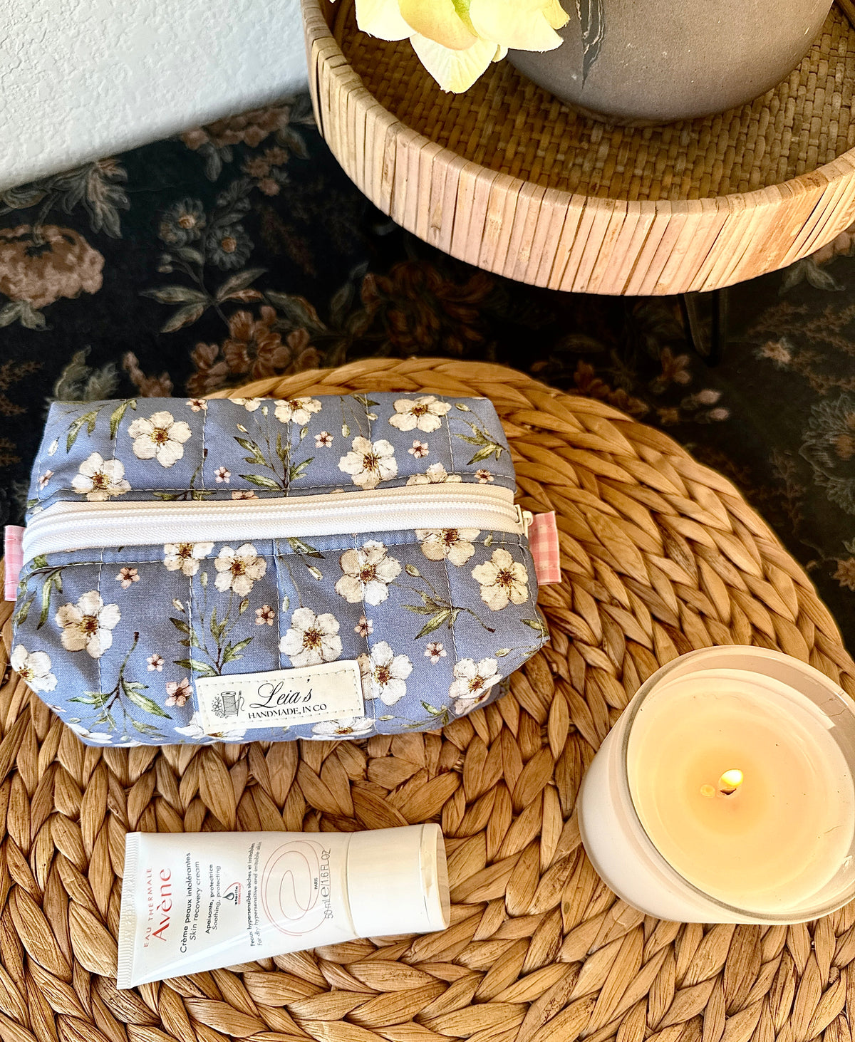 Small blue floral quilted boxy bag with white zipper and pink side tabs, styled with skincare