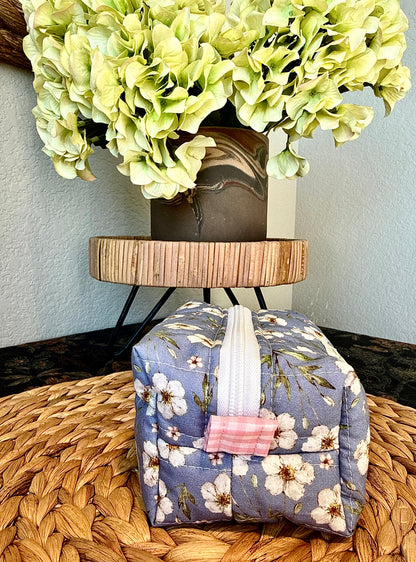 Side view of small blue floral quilted boxy bag showing its white zipper and pink side tab