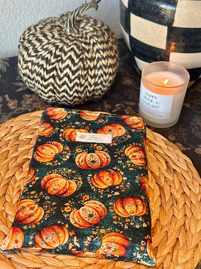 Overhead view of handmade quilted book sleeve in dark teal Gilded Gourd pumpkin print on a wicker charger with fall décor
