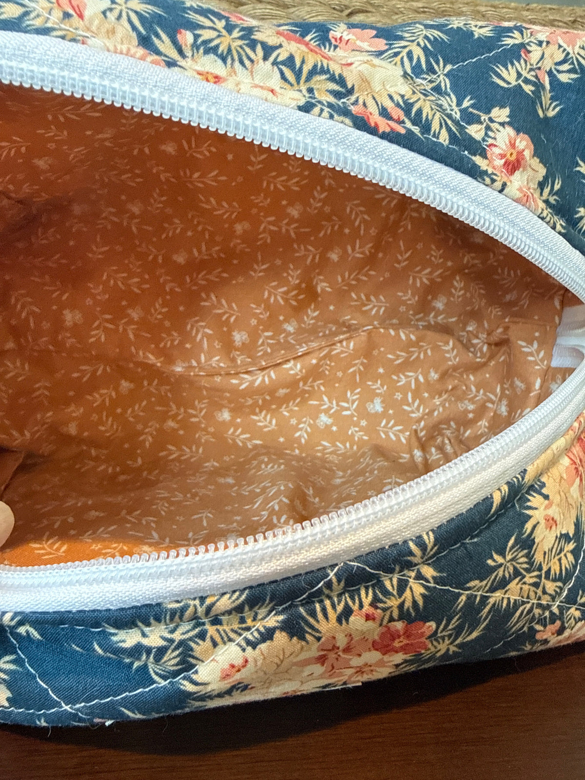Close-up of a zippered pouch or bag with a navy floral exterior and a tan patterned interior, shown on a wooden surface.