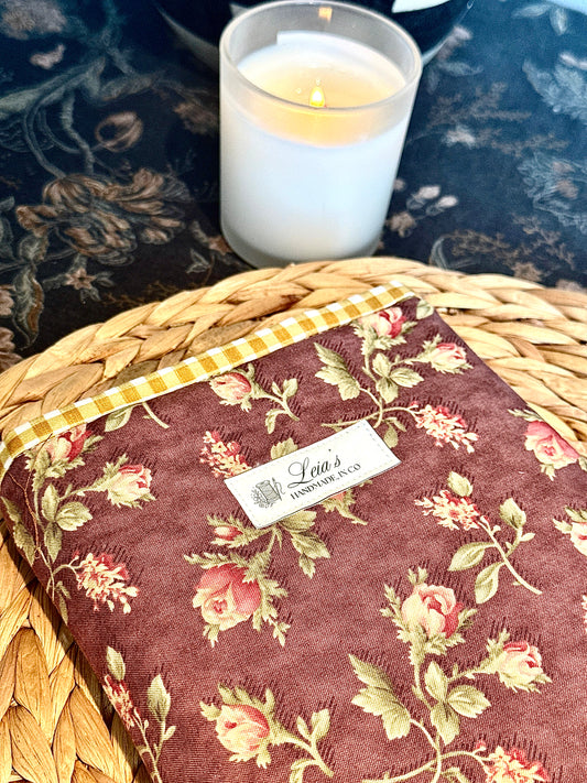 Close-up of Leia's handmade label on rosewood floral quilted book sleeve resting on wicker surface with lit candle