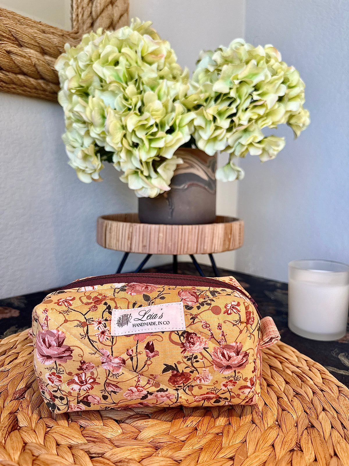 Small golden floral quilted boxy bag with pink roses displayed on a woven tray