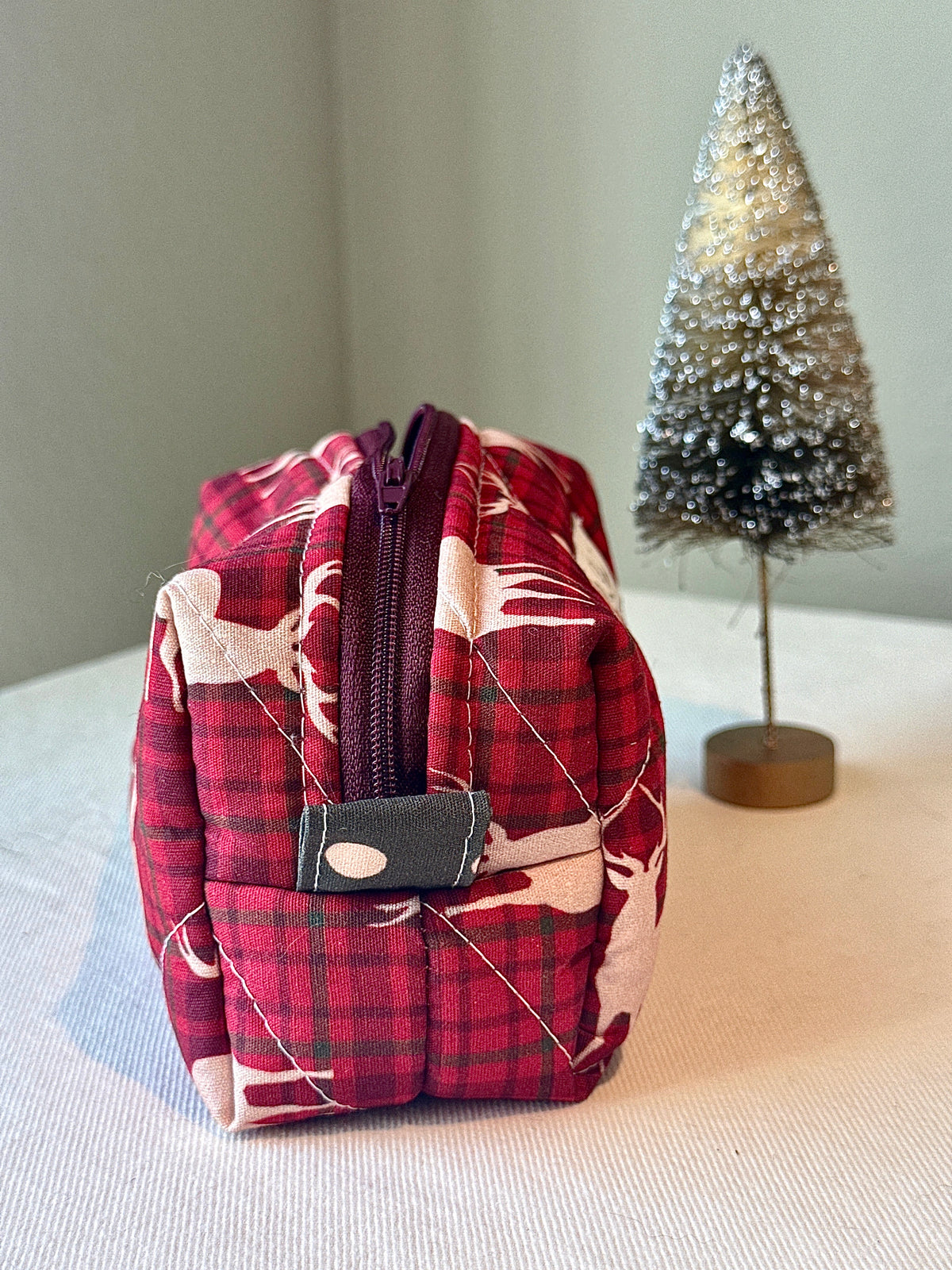 Side view of the red plaid stag-print bag showing its zipper and pull tab