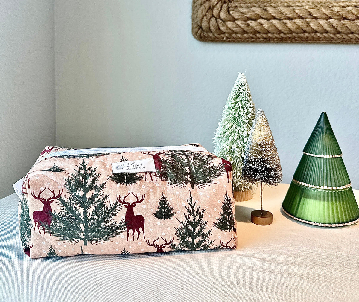Winter Stag boxy bag showing its deer-and-evergreen print, displayed beside three decorative trees.