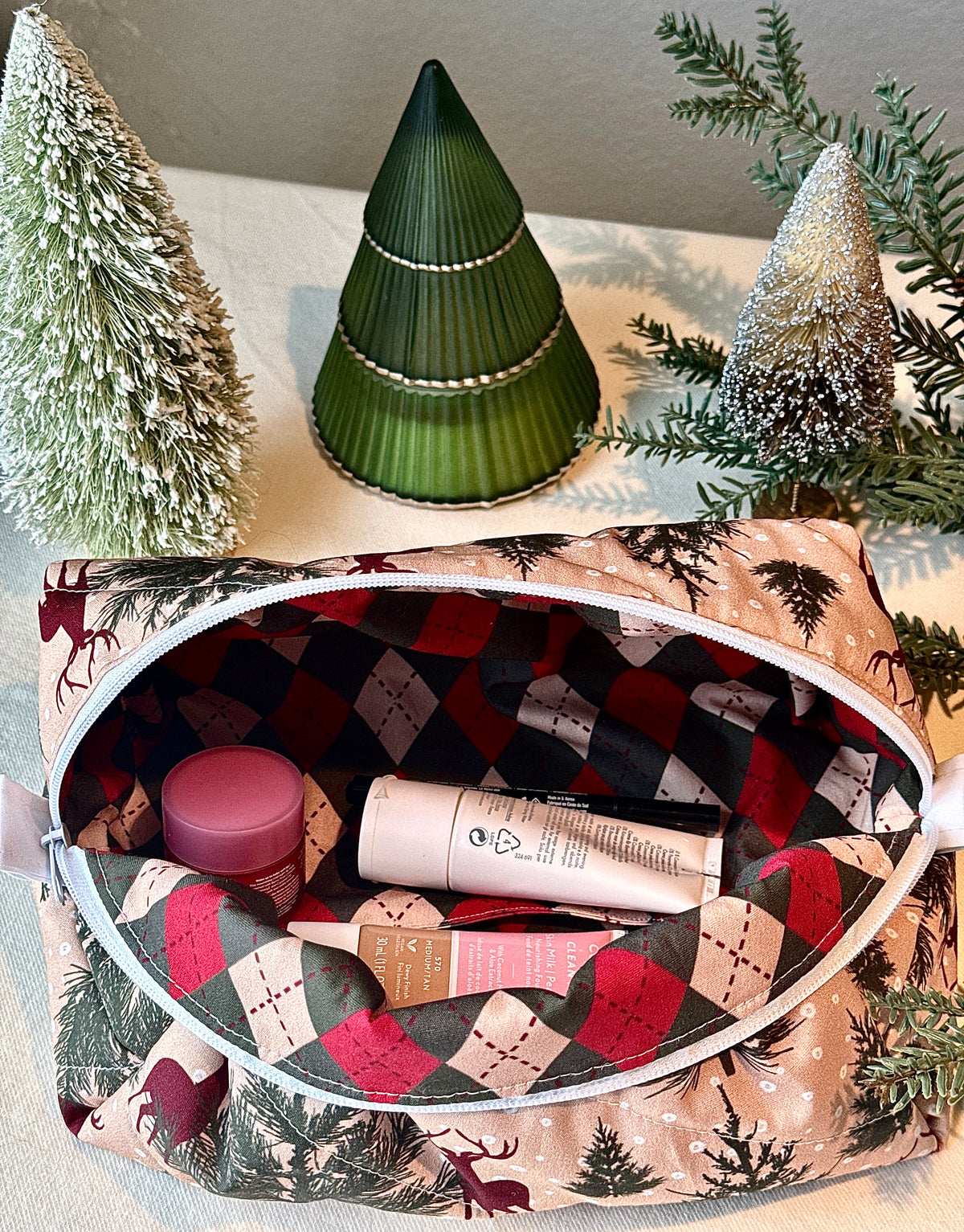 Open Winter Stag boxy bag holding toiletries, with its red, green, and cream patterned lining visible.