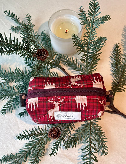 Top-down view of the red plaid stag-print boxy bag styled among evergreen branches and a candle