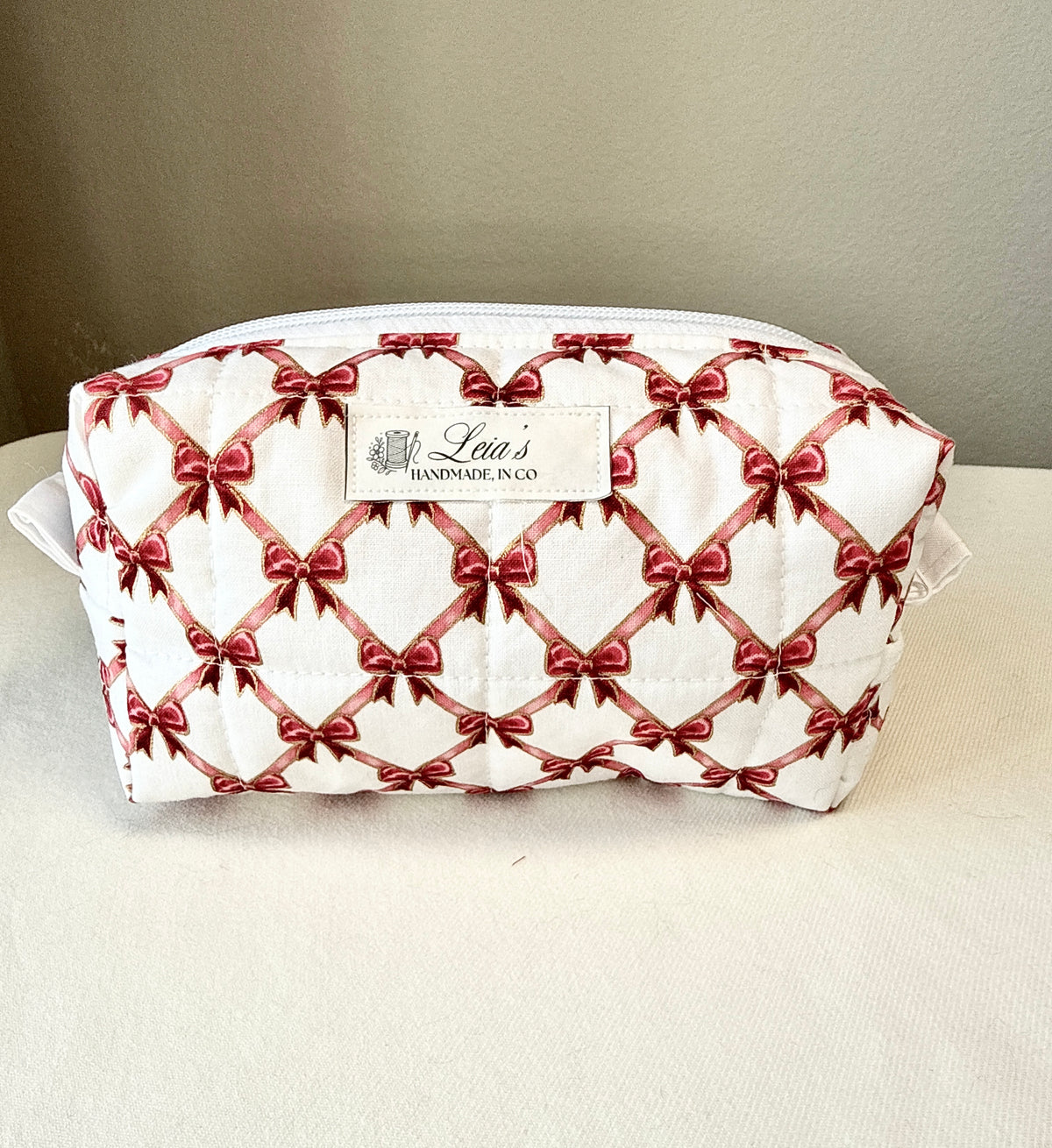 A quilted white cosmetic pouch with a repeating red bow pattern.